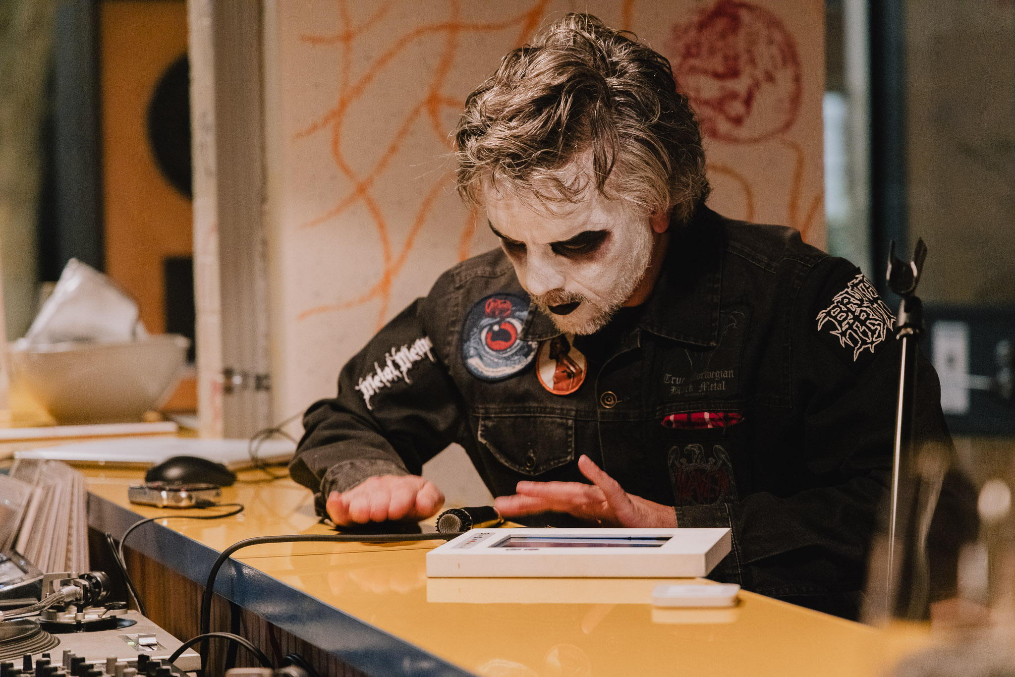 image of a person dressed up with white paint on his face and a leather jacket. He's touching the microphone.